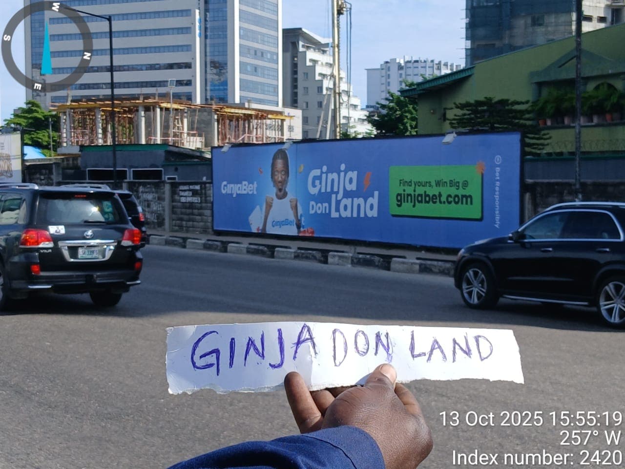 GinjaBet billboard on Victoria Island, photographed with a dated site-verification card held to camera.