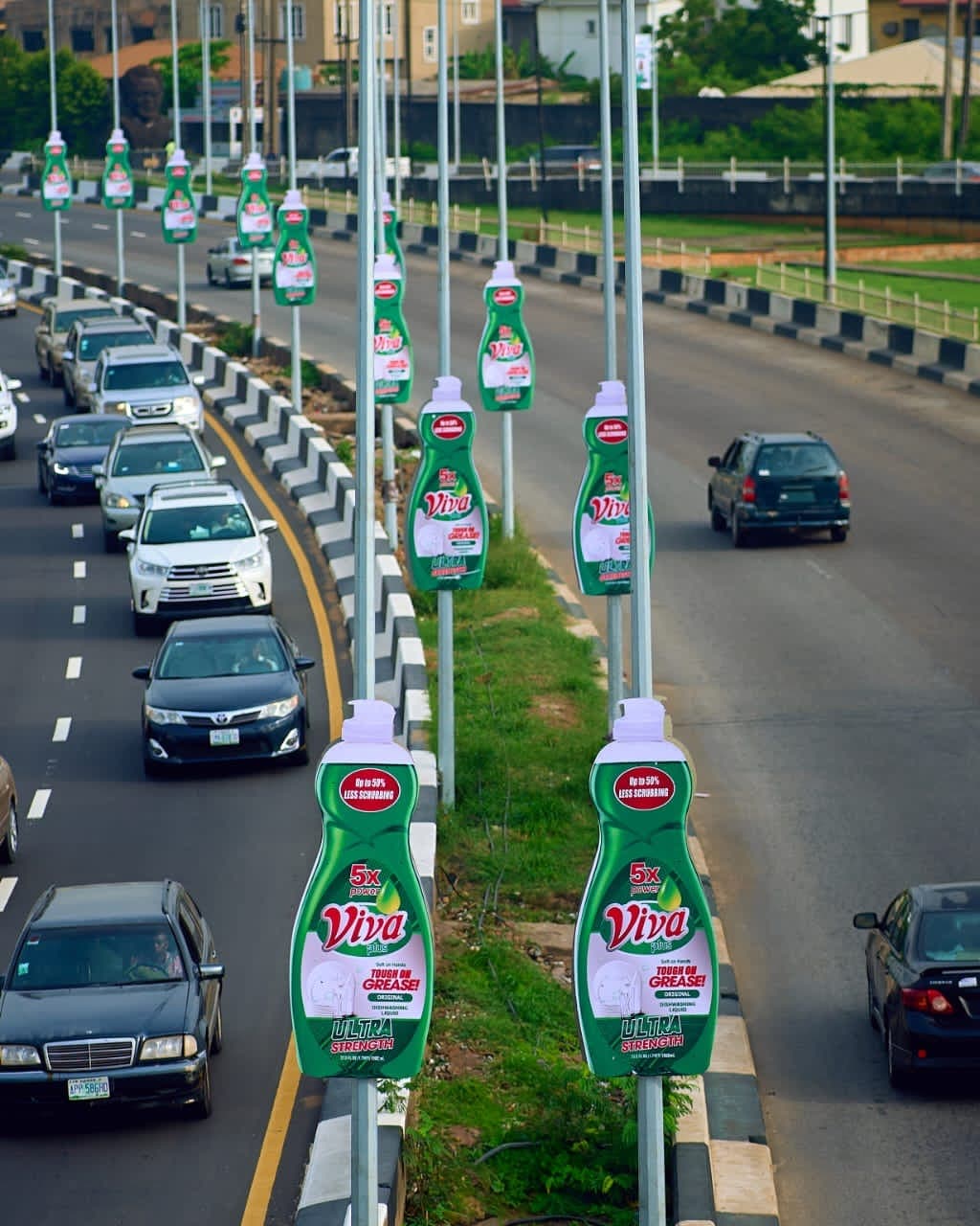 A long run of Viva dishwashing liquid median poles down the central reservation of a Lagos dual carriageway, shaped as the bottle.