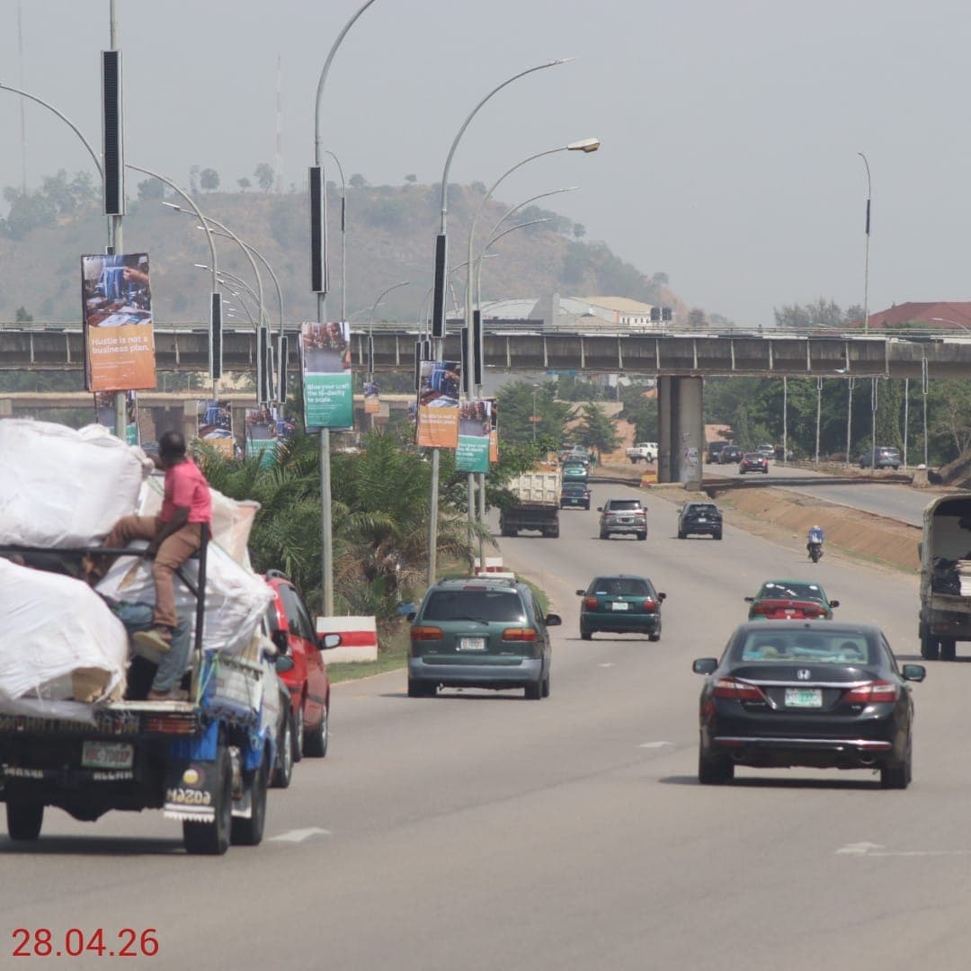 Banner panels on street-light columns along an Abuja expressway, carrying a small business campaign.